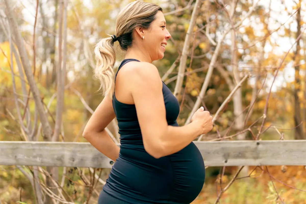 Schwangere Frau joggt entspannt im Profil durch herbstliche Natur